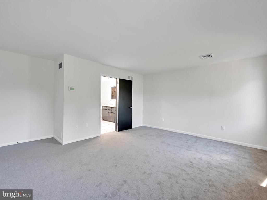 Empty carpeted room with white walls and an open doorway to the kitchen.