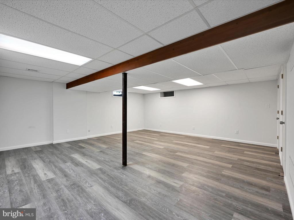 Finished basement with gray plank flooring and a dark ceiling beam supported by a post.