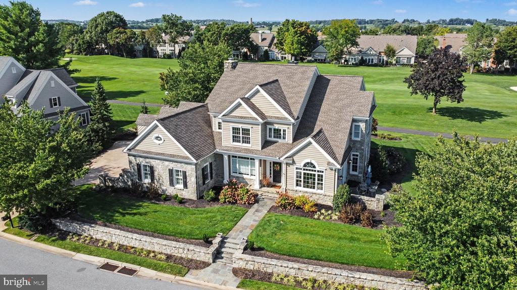 Aerial view of a stone-fronted home with landscaped lawn and broad community greenspace.