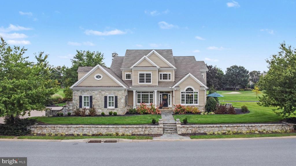 Two-story stone-and-siding home with multiple gables, landscaped lawn, and golf course behind it.