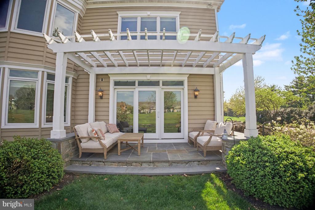 Home’s rear patio with a white pergola, stone steps, and furnished seating.