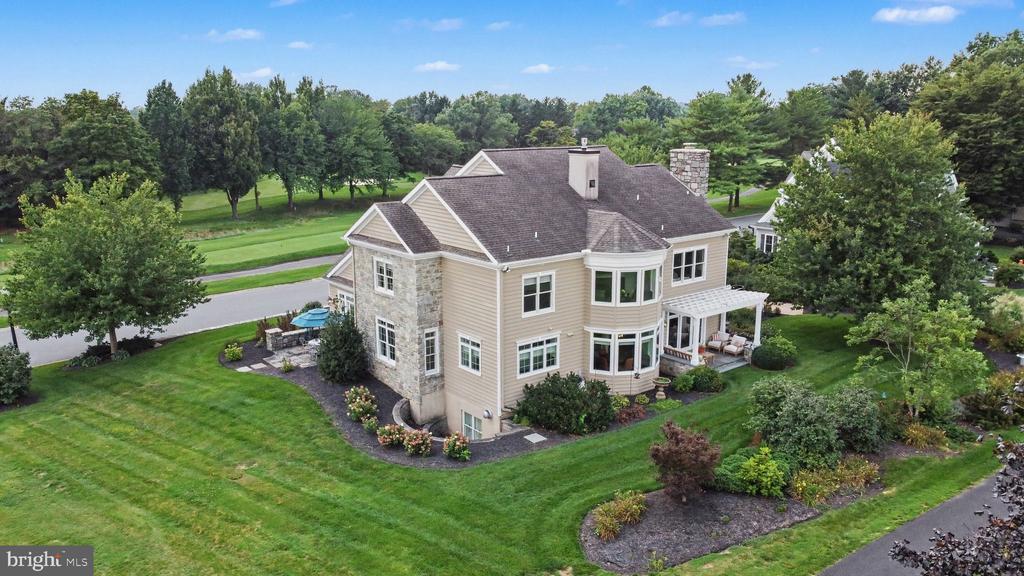 Aerial view of a beige two-story home with stone accents, bay windows, and landscaped grounds.