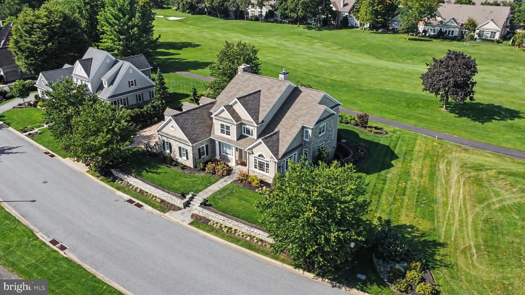 Aerial view of a gray stone-and-siding home beside a broad green lawn and paved path.