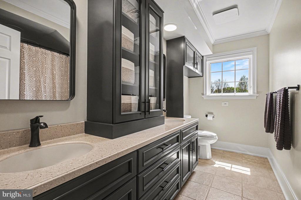 Bathroom with a dark double vanity, glass-front cabinets, and a bright window.