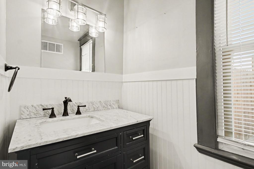 Bathroom with a dark vanity, marble countertop, black faucet, beadboard walls, and a large mirror.