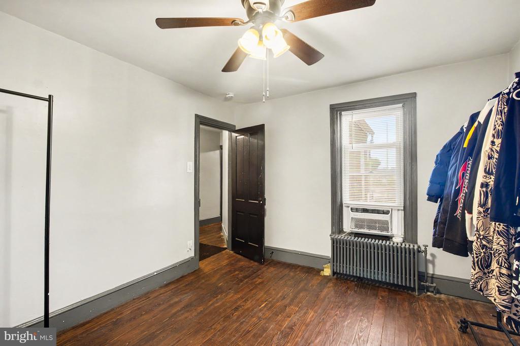 Bedroom with dark hardwood floors, a ceiling fan, and a window air conditioner above a radiator.