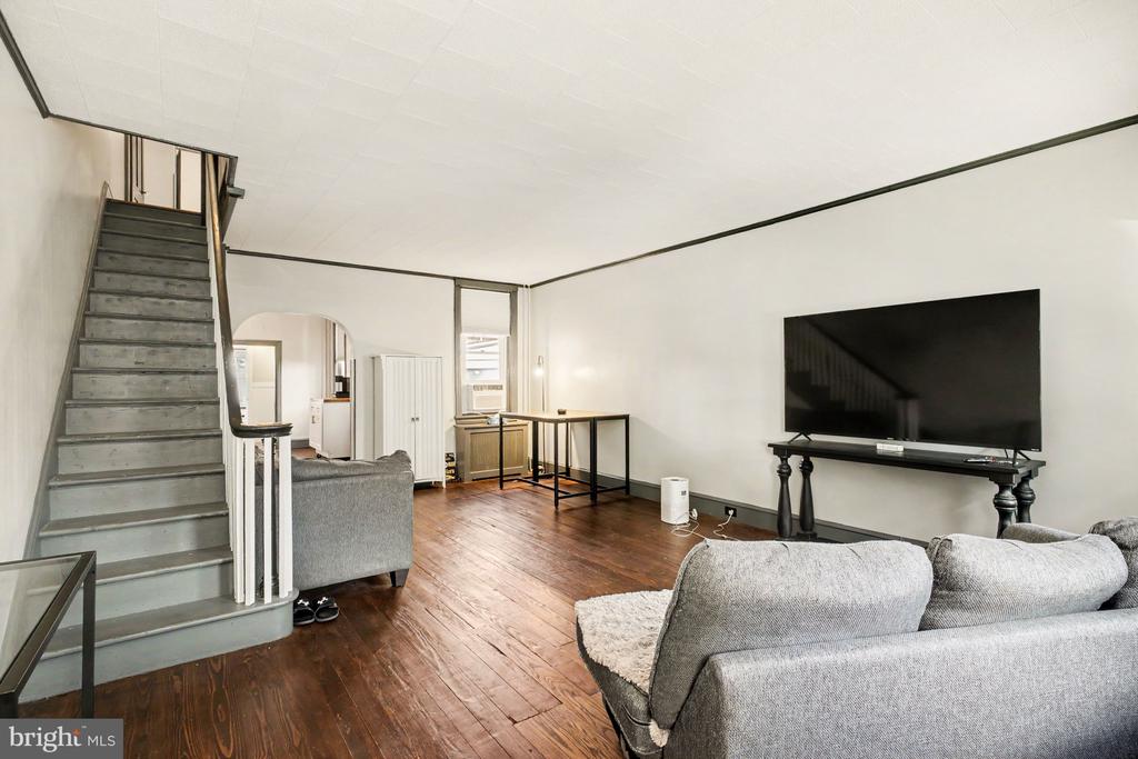 Living room with dark wood floors, gray sofas, and a staircase beside the seating area.