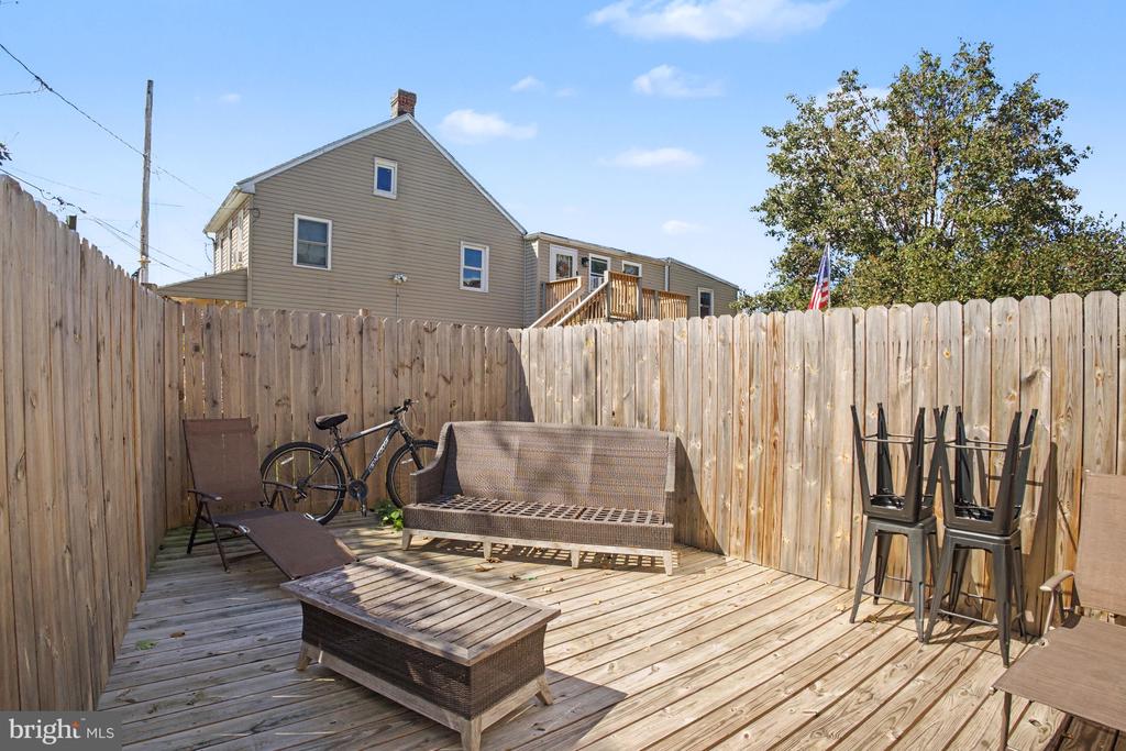 Fenced backyard deck with outdoor seating and a bicycle, with the house visible beyond the fence.