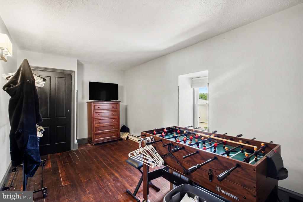 Recreation room with a foosball table, dark hardwood floors, and a dresser topped by a television.