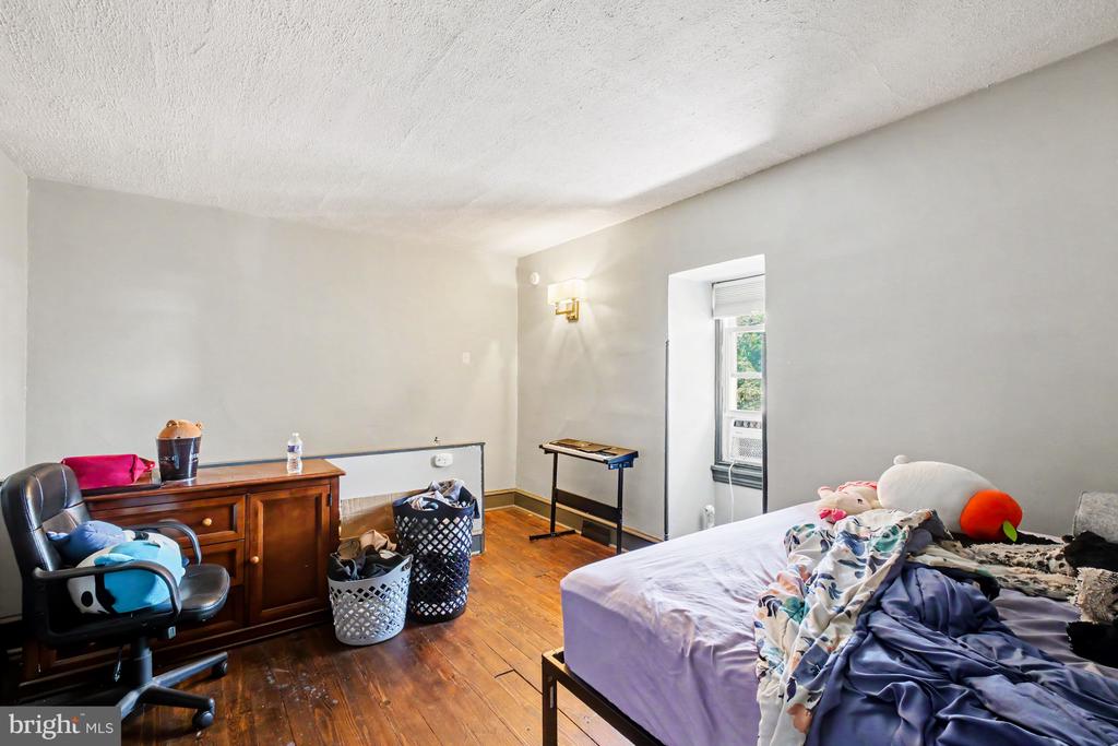 Bedroom with hardwood floors, a bed, dresser, and window air conditioner.
