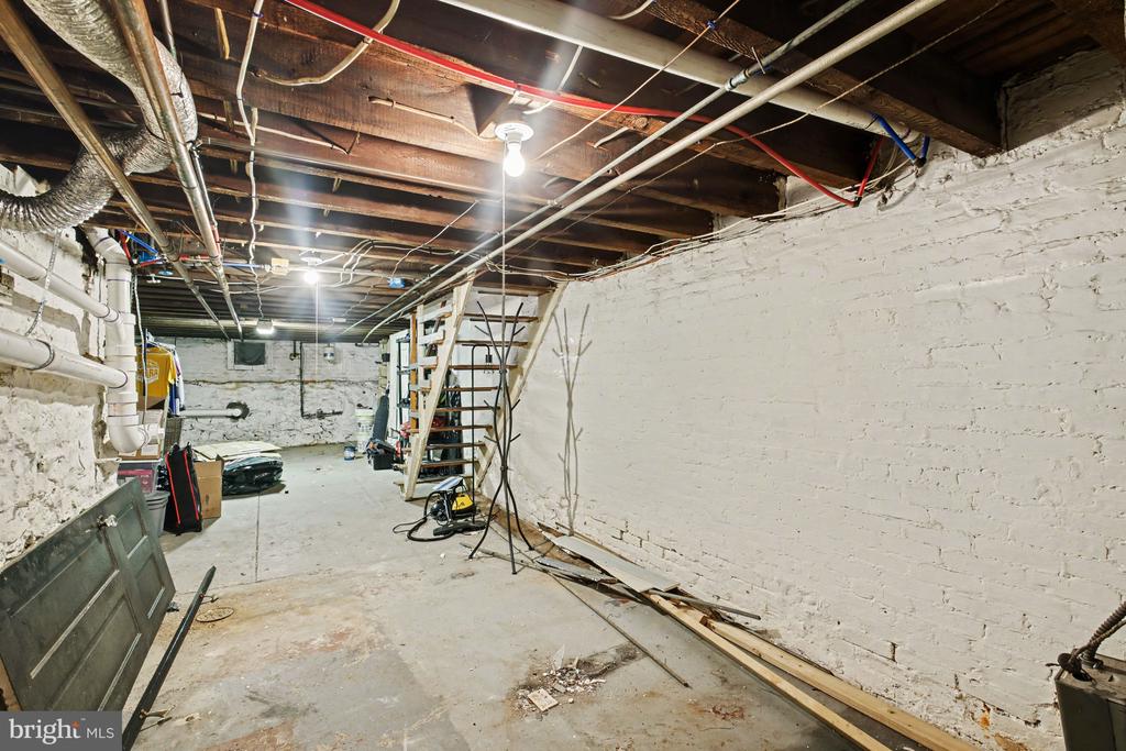 Unfinished basement with white brick walls, exposed ceiling joists, utility pipes, and a concrete floor.