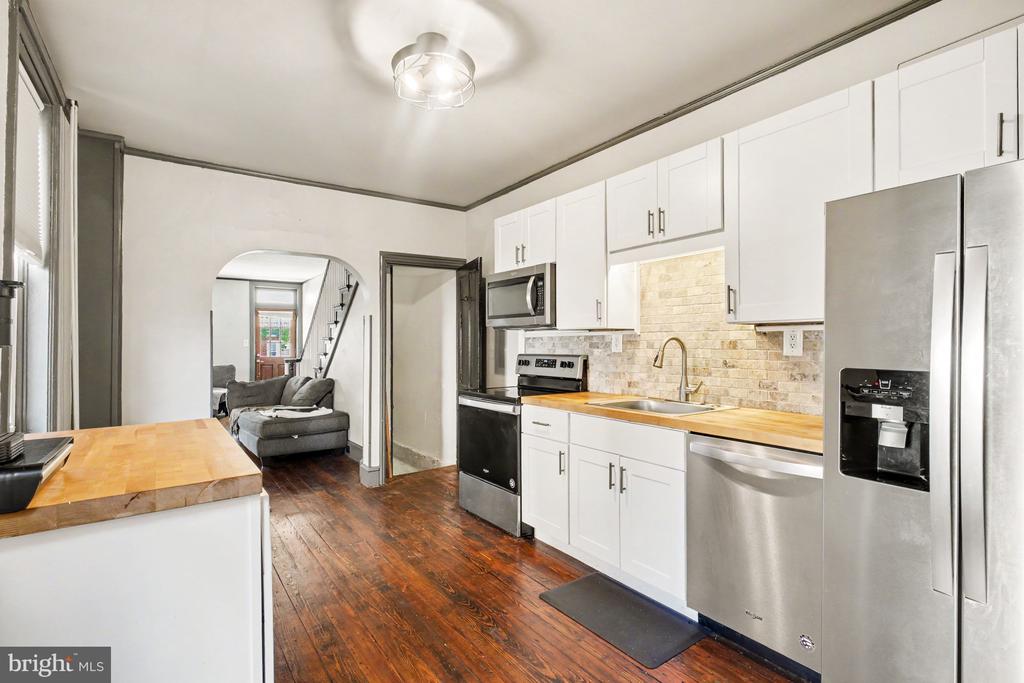Kitchen with white cabinets, stainless steel appliances, butcher-block counters, and an arched opening to the living room.