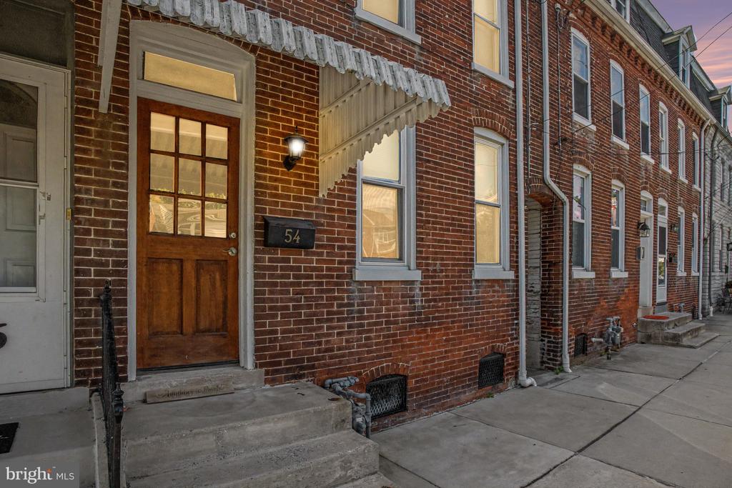 Red-brick row house entrance with wooden door, stone steps, and a 54 address plaque.