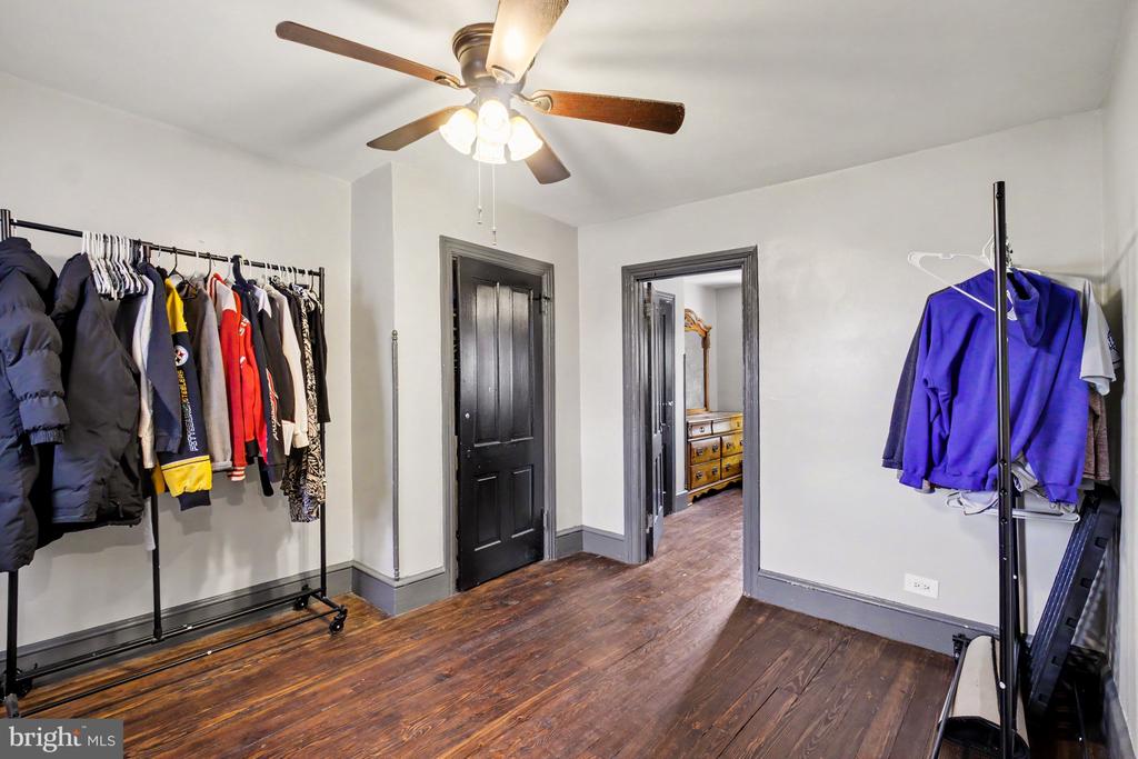 Clothing storage room with garment racks, dark hardwood floors, and a ceiling fan.