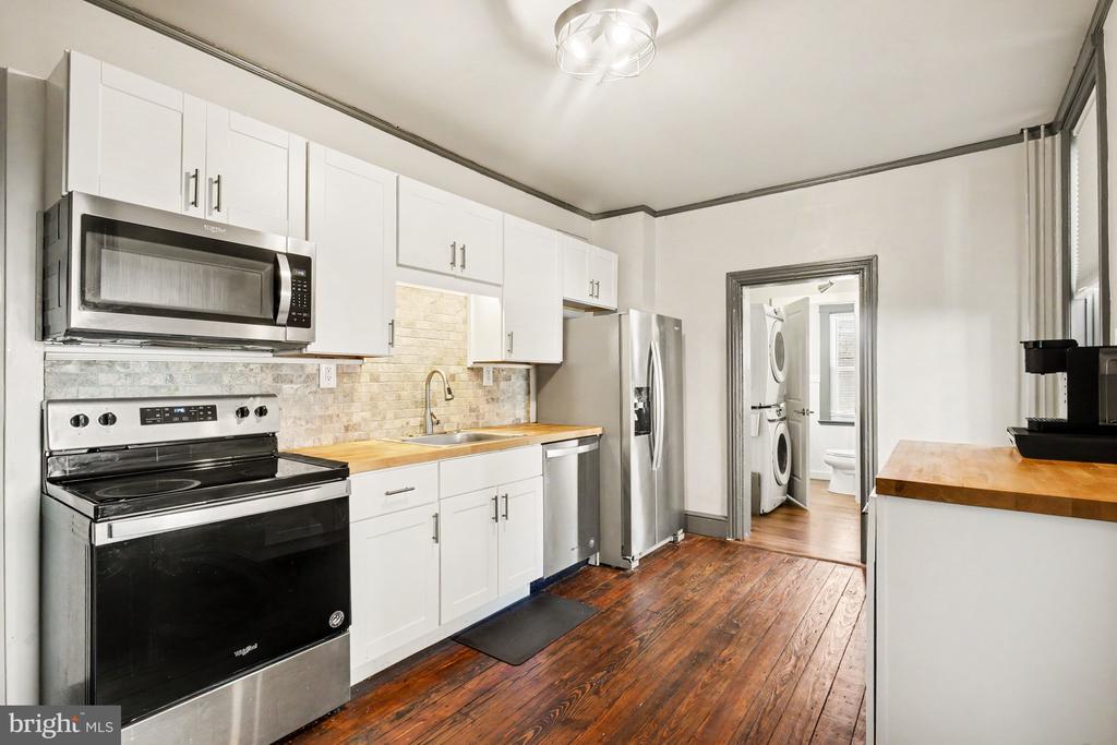 Kitchen with white cabinetry, stainless steel appliances, butcher-block counters, and dark wood flooring.