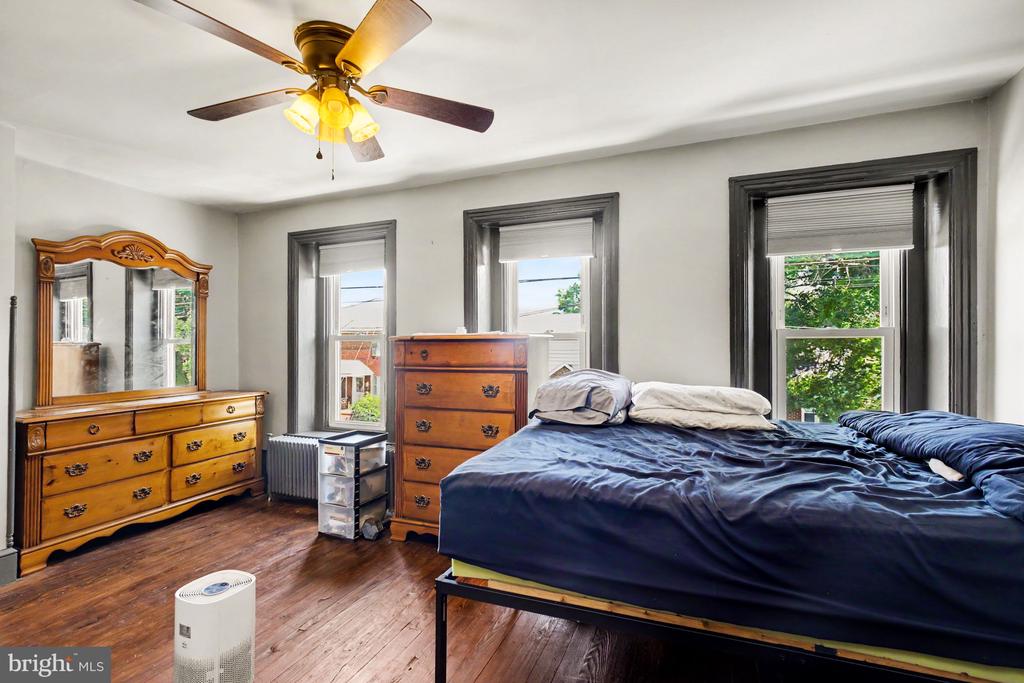 Bedroom with hardwood floors, dark-trimmed windows, wooden dressers, and a large bed.