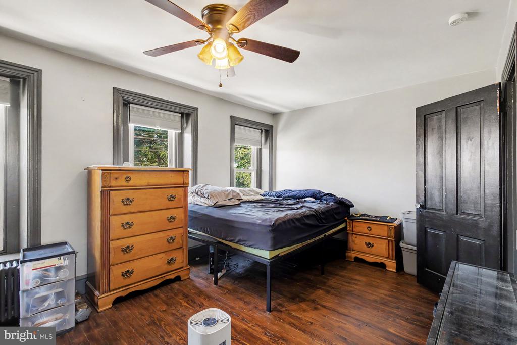 Bedroom with a bed, wooden dressers, dark hardwood floors, and a ceiling fan.