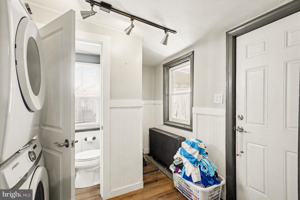 Laundry room with stacked washer and dryer, a full laundry basket, and an adjacent bathroom.