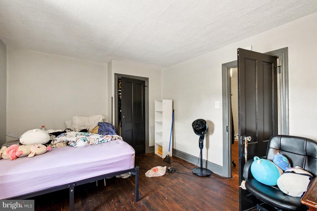 Bedroom with a rumpled bed, plush toys, dark wood floors, and open black doors.