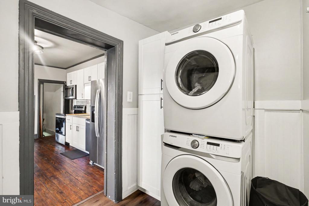 Laundry area with stacked front-load washer and dryer beside a doorway to the kitchen.