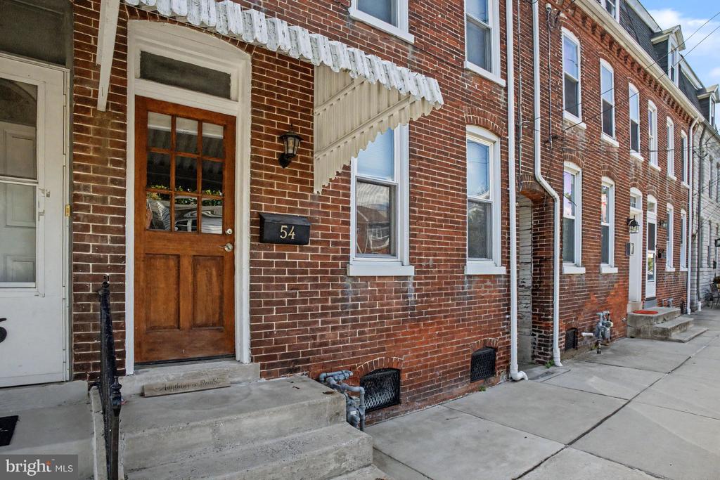 Red-brick rowhouse with a wooden entrance door, white awning, and concrete steps.