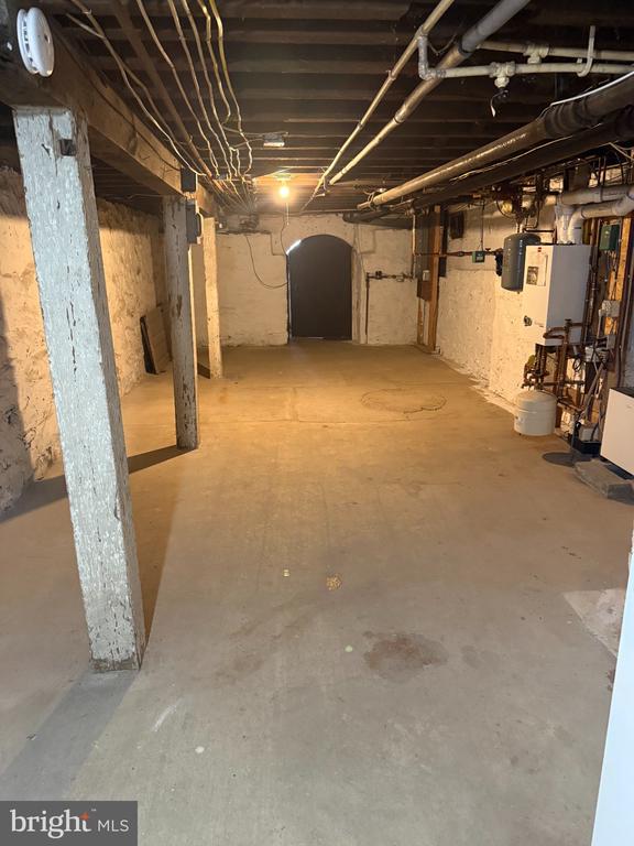 Unfinished basement with exposed pipes, support posts, and utility equipment.