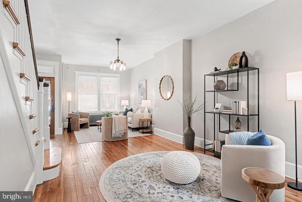 Furnished living room with polished hardwood floors, large windows, neutral seating, and a black metal display shelf.
