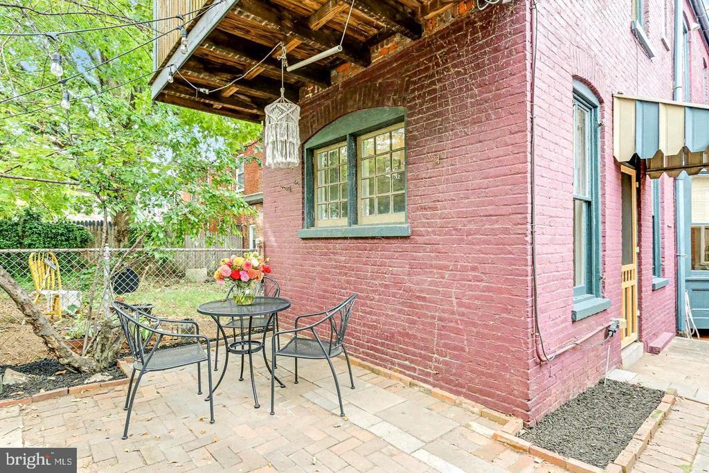 Brick patio with metal table and chairs beside a red brick house under a wooden awning.