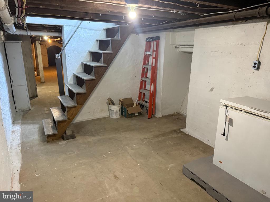 Unfinished basement with an open wooden staircase, exposed ceiling joists, and utility equipment.
