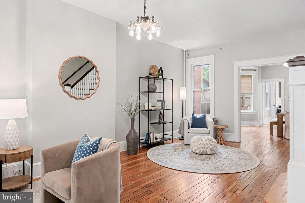Living room with polished hardwood floors, a round rug, upholstered seating, and black open shelving.
