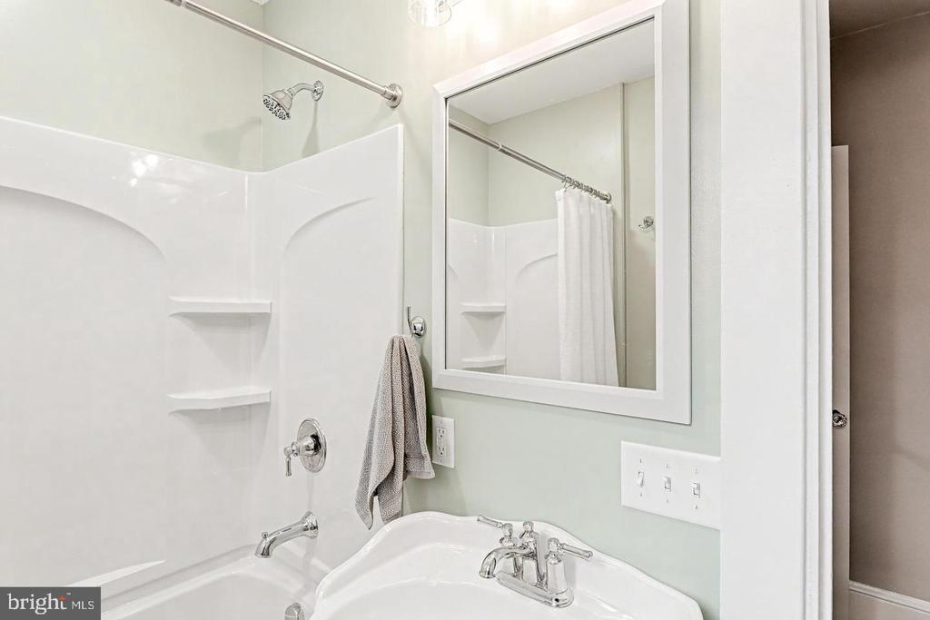 Bathroom with a white tub-shower, built-in corner shelves, and a single-sink vanity.