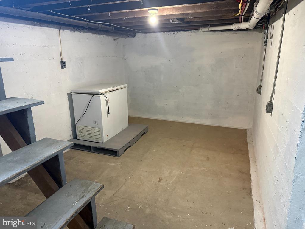 Unfinished basement with a chest freezer, exposed joists, and stairs along one side.