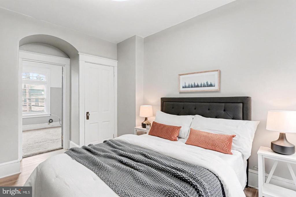 Staged bedroom with a white bed, charcoal tufted headboard, and arched doorway.