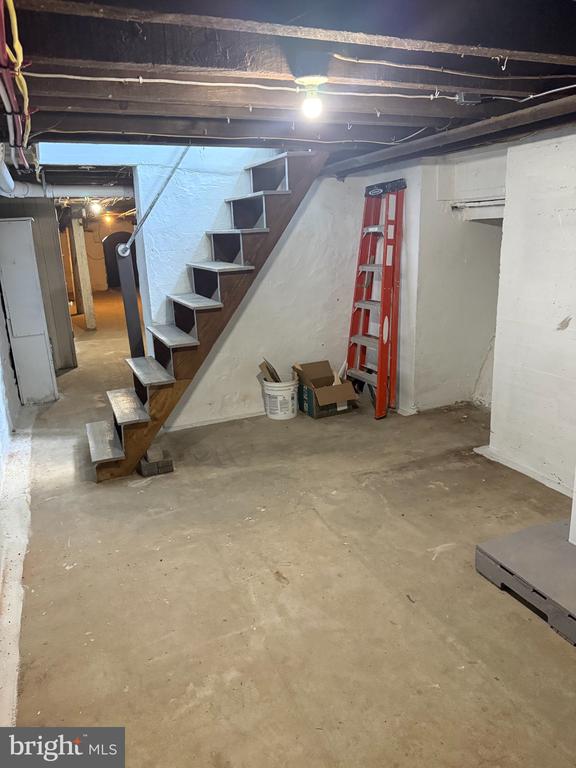 Unfinished basement with exposed ceiling joists, a concrete floor, and an open wooden staircase.