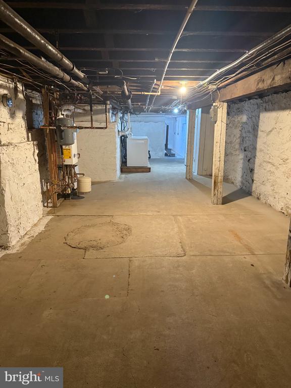 Unfinished basement with exposed pipes, utility equipment, and a wide concrete floor.