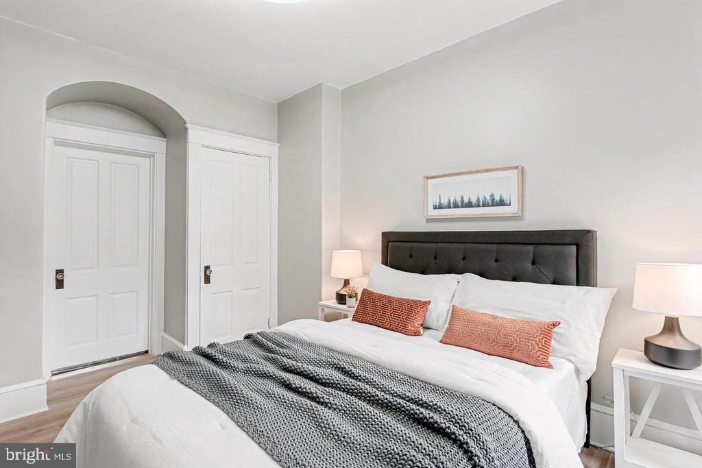 Staged bedroom with a charcoal tufted headboard, rust-colored pillows, and an arched alcove over one door.