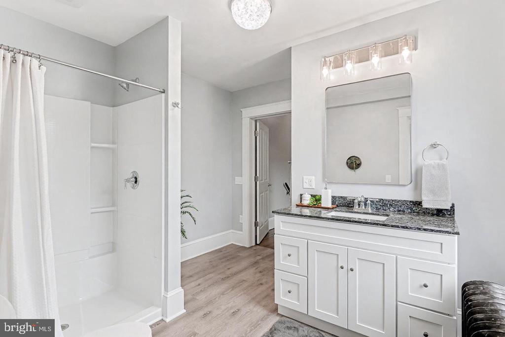 Bathroom with a white tub and shower, paneled vanity, dark countertop, and wood-look flooring.
