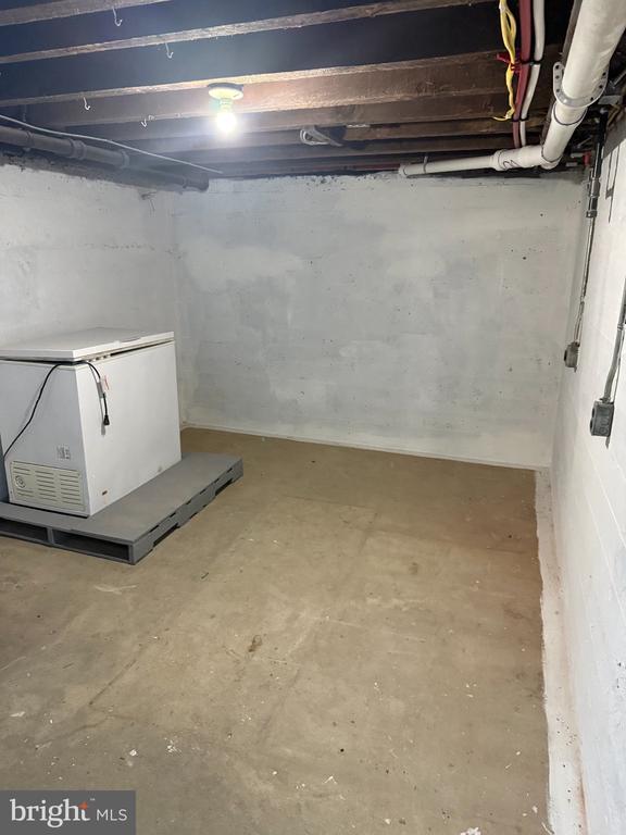 Unfinished basement with exposed ceiling pipes and a large white utility appliance on a platform.