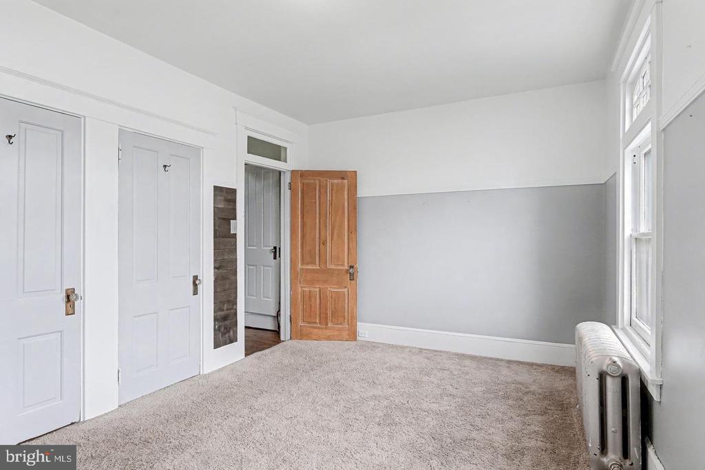Empty carpeted room with gray-and-white walls, paneled doors, tall windows, and a radiator.