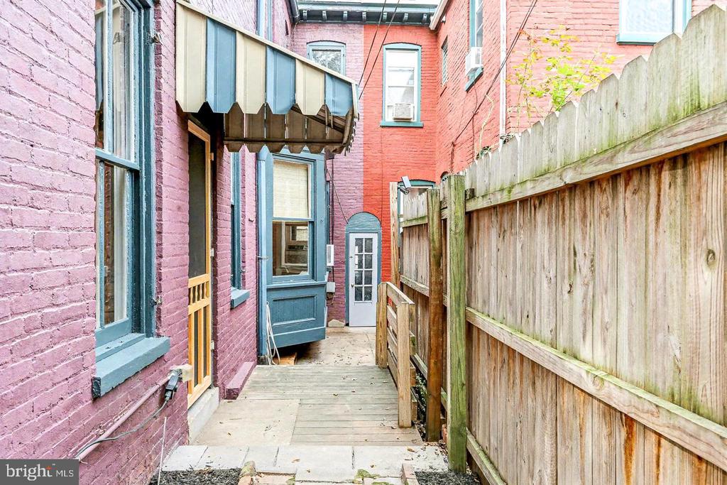 Narrow wooden walkway beside painted brick walls, leading to a blue-trimmed rear door.