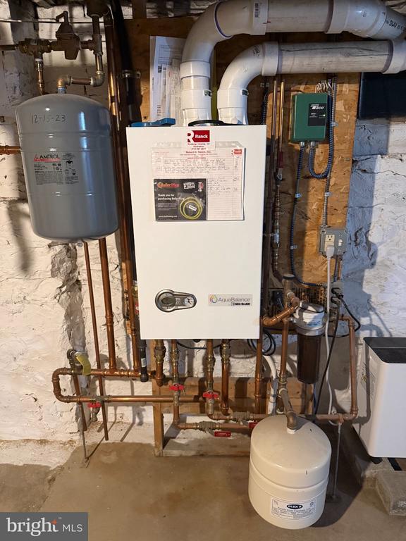 Basement utility room with a wall-mounted boiler, exposed plumbing, and expansion tanks.