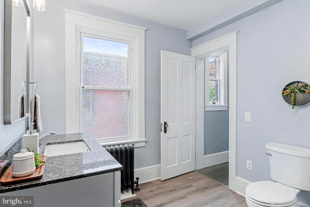 Bathroom with a gray stone vanity, white toilet, black radiator, and open doorway.