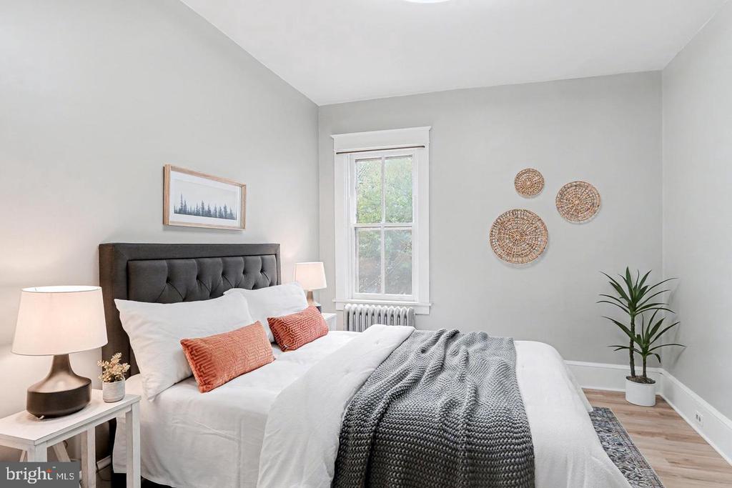 Staged bedroom with a tufted headboard, rust-colored pillows, gray knitted throw, and window above a radiator.