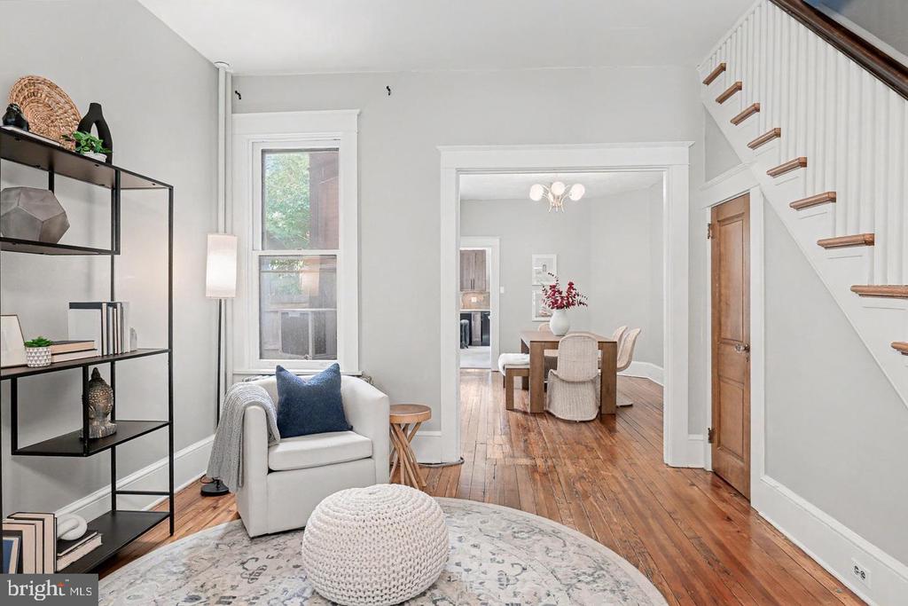 Staged living room with a white armchair, hardwood floors, and an open view into the dining room.