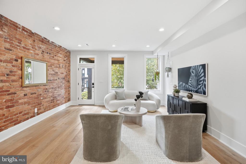 Staged living room with an exposed brick wall, pale wood floors, and sculptural white sofa.