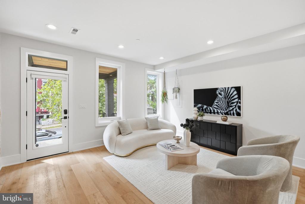 Staged living room with a curved cream sofa, tall windows, and pale wood floors.