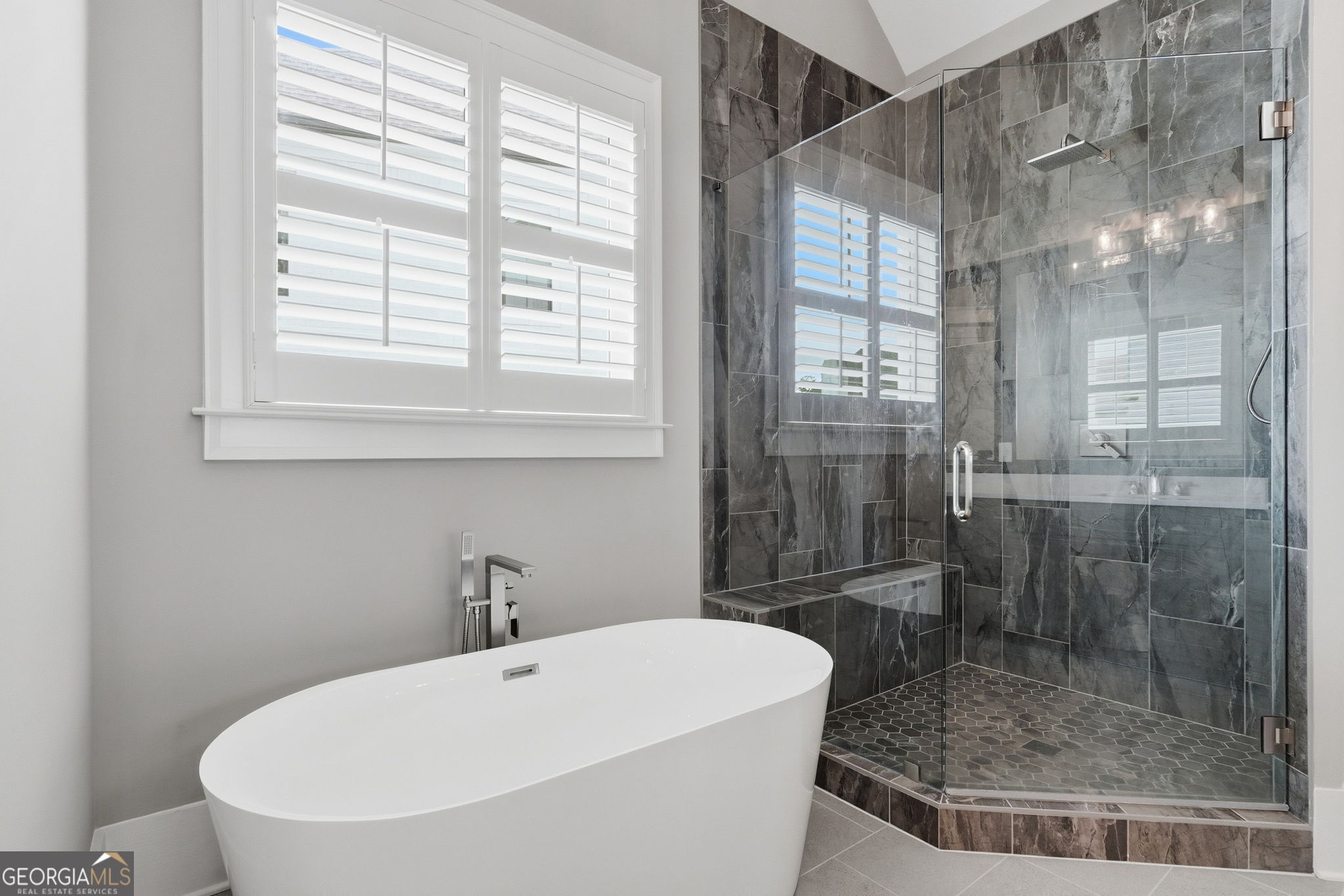 Modern bathroom with a freestanding soaking tub and dark stone-tiled glass shower.