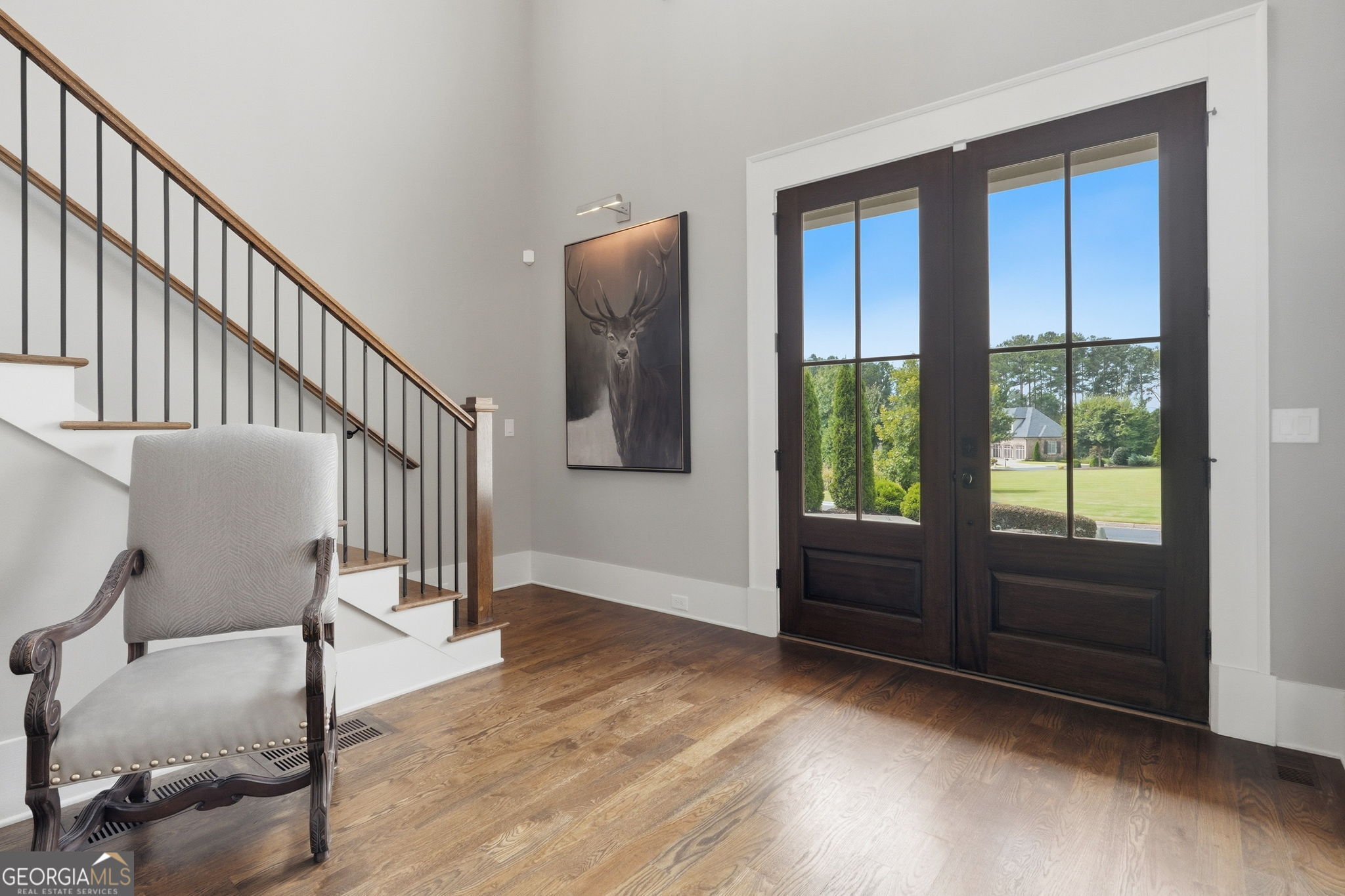 Entry foyer with hardwood floors, dark double doors, a staircase, and an upholstered chair.