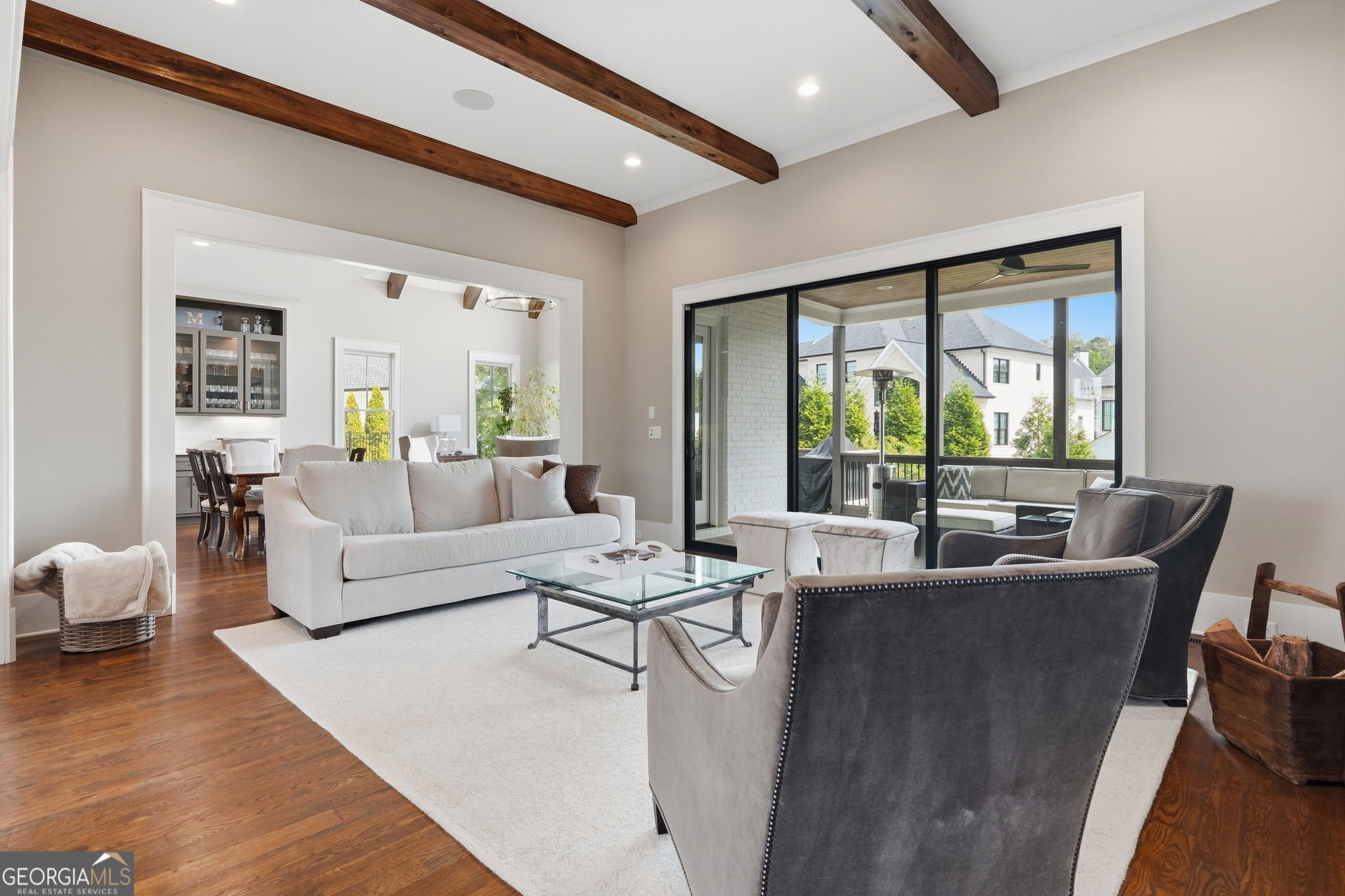 Staged living room with exposed wood beams, hardwood floors, and sliding glass doors to a covered patio.