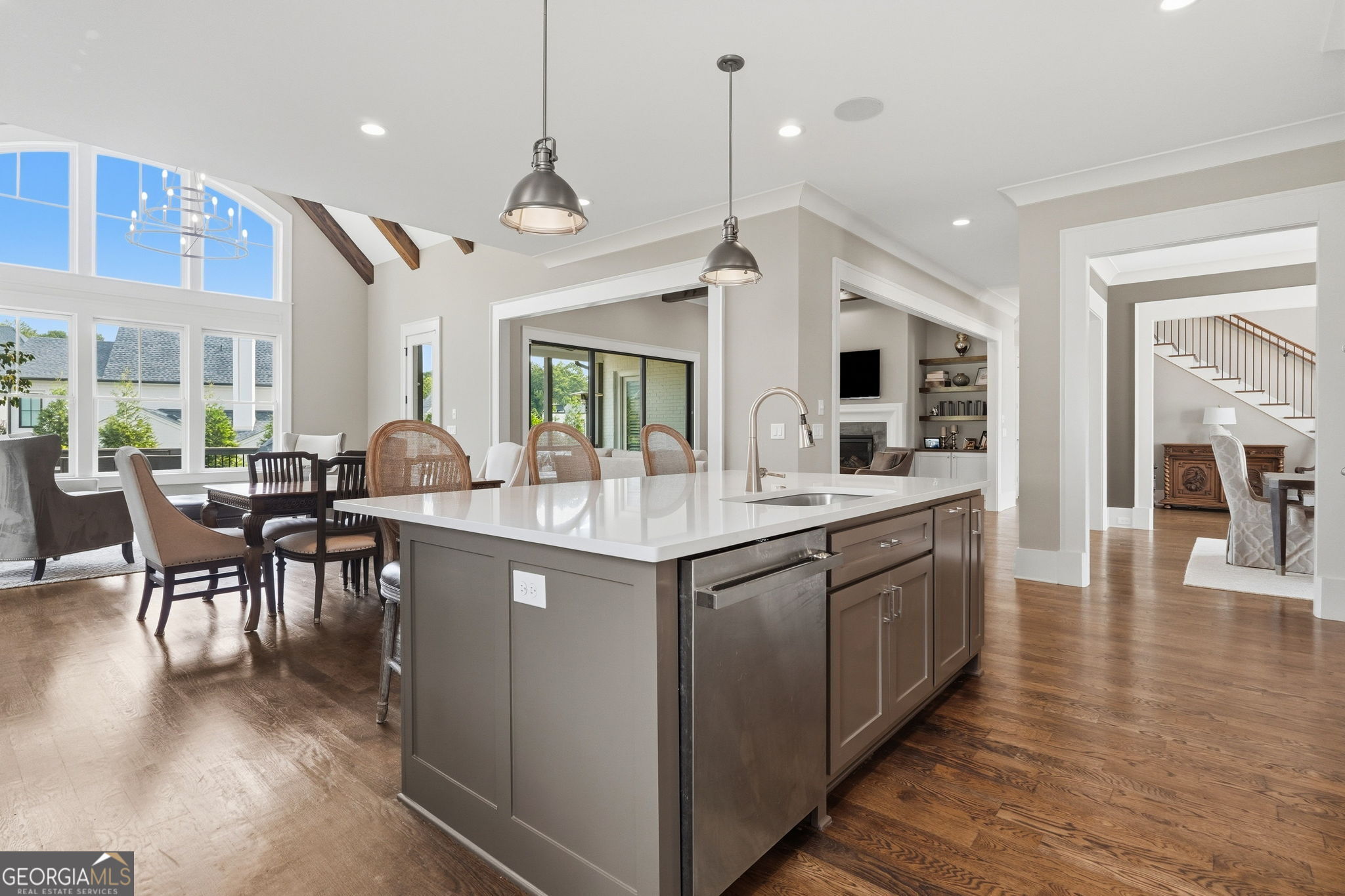 Open kitchen with a large white-topped island, stainless dishwasher, tall windows, and adjoining dining and living areas.